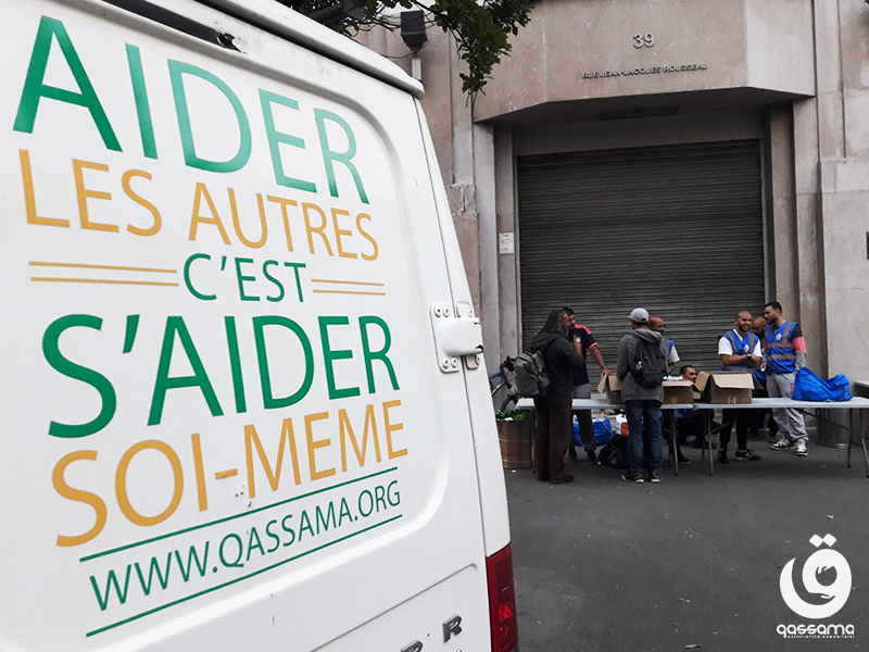 Camionette avec le slogan de l'association, "aider les autres c'est s'aider soi-même", devant un groupe de bénévoles et bénéficiaires